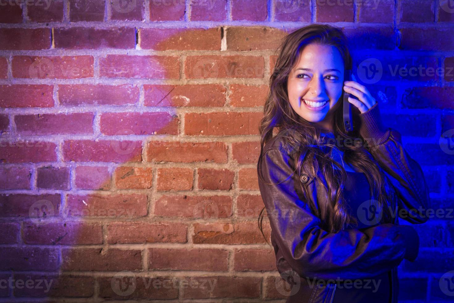 Mischlingsfrau, die ihr Handy gegen die Mauer benutzt foto