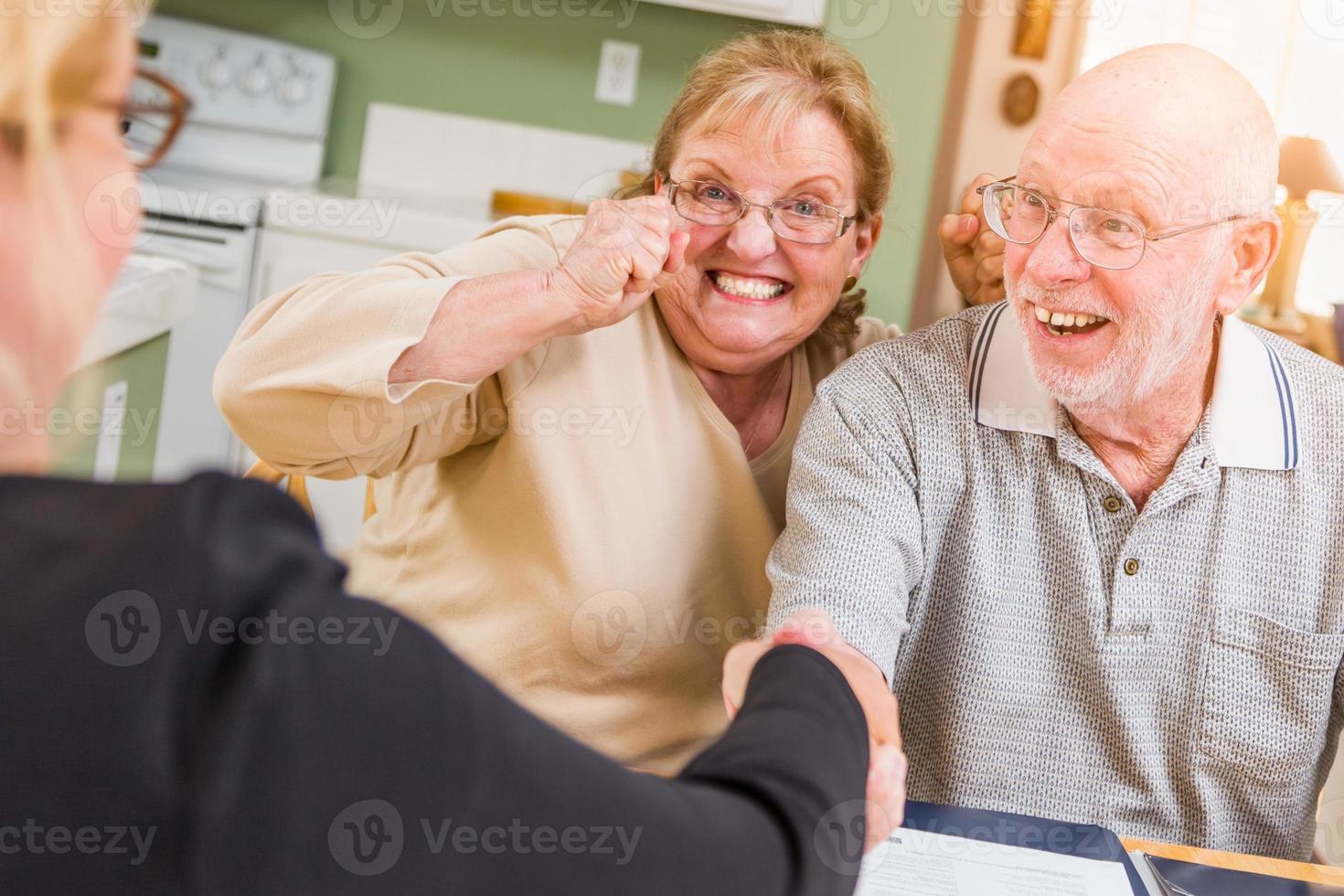 älteres erwachsenes paar, das über dokumente in ihrem haus mit agent bei der unterzeichnung feiert foto