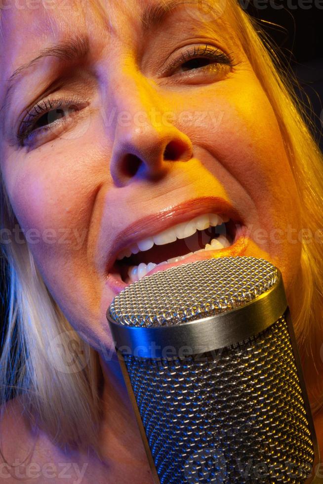 Sängerin unter Gellicht singt mit Leidenschaft in ein Kondensatormikrofon. foto