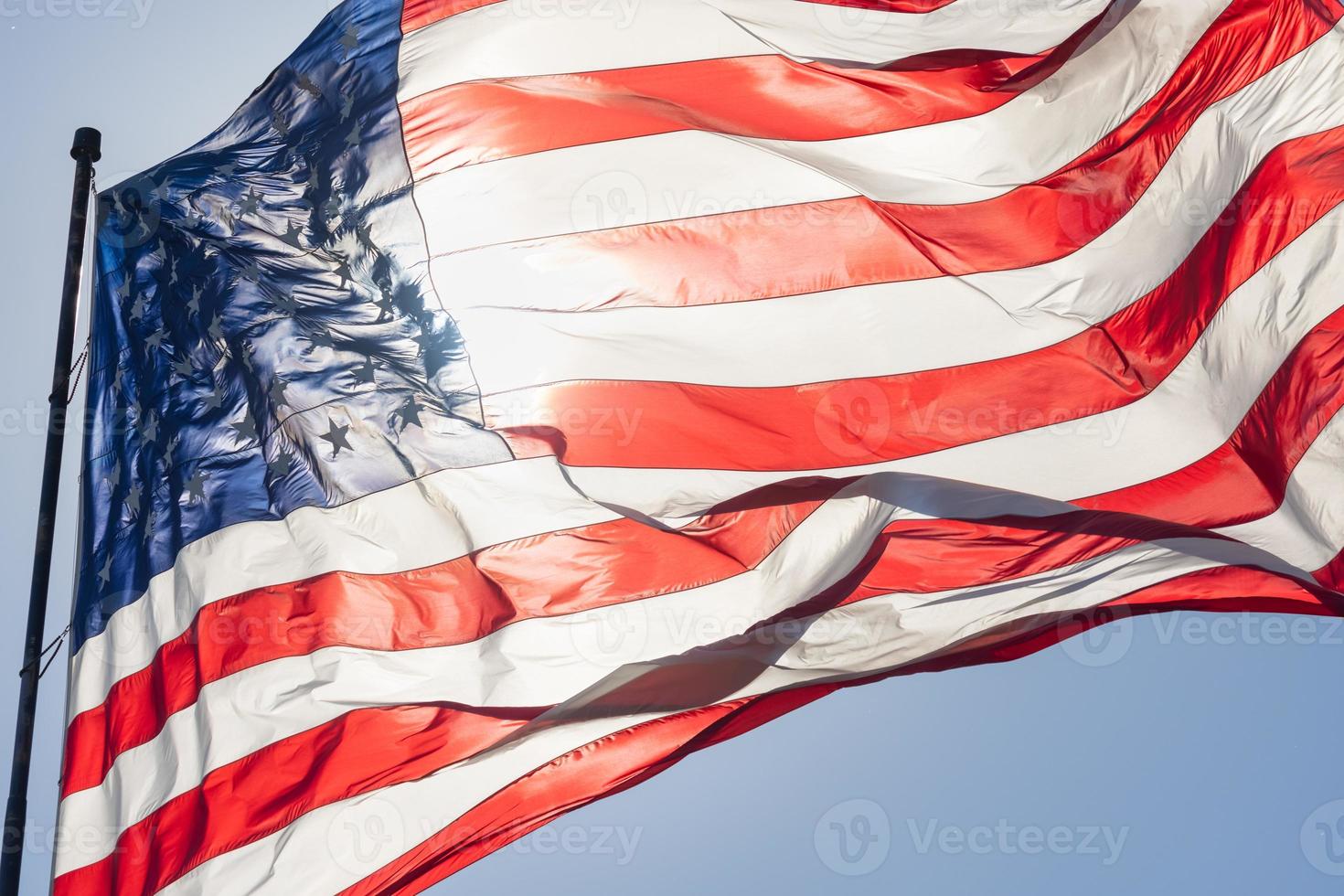 hintergrundbeleuchtete amerikanische flagge, die im wind gegen einen tiefblauen himmel weht foto