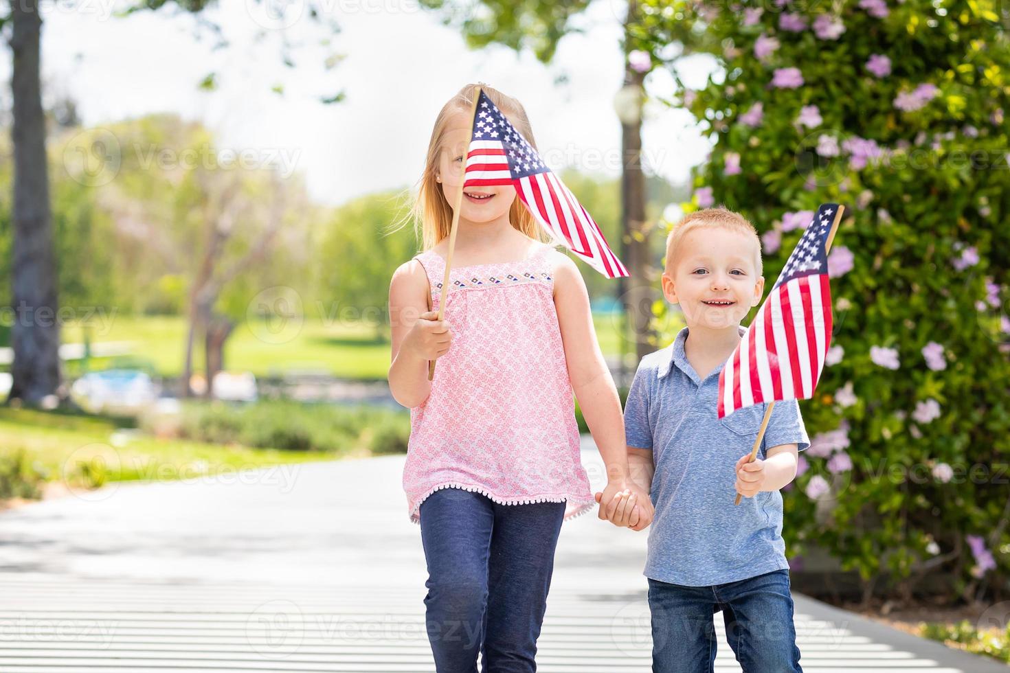 junge schwester und bruder schwenken amerikanische flaggen im park foto