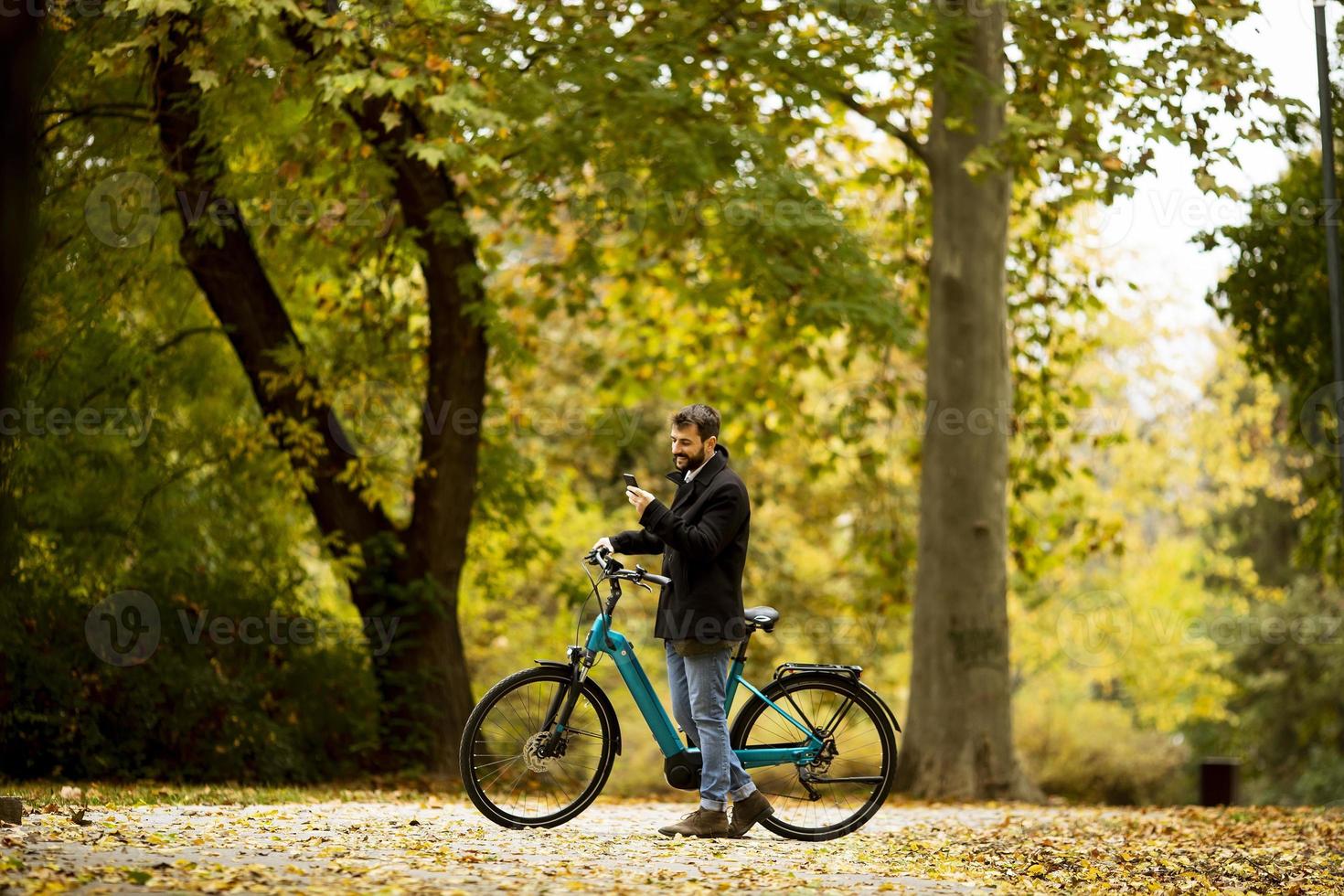 hübscher junger Mann mit Elektrofahrrad im Herbstpark foto