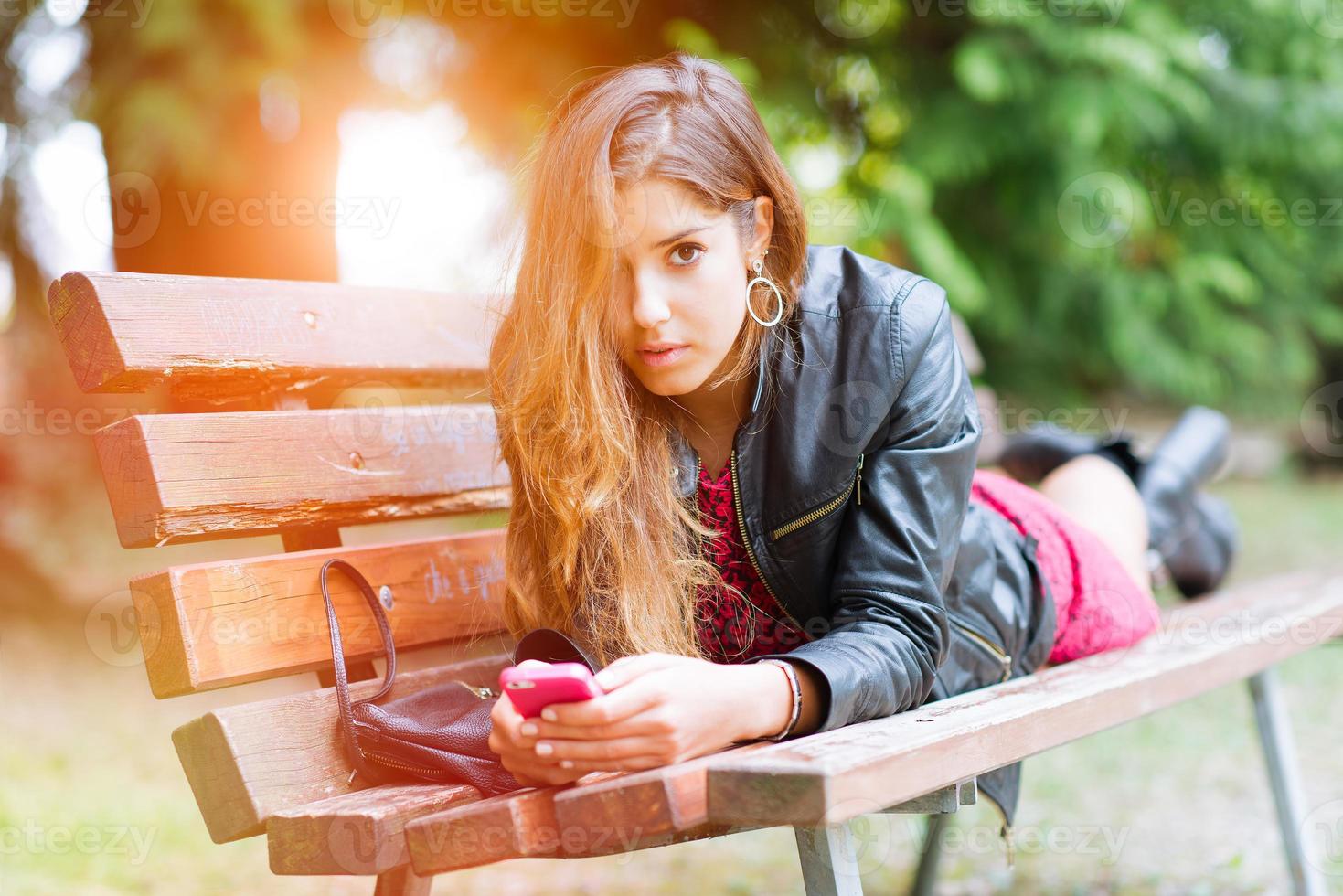 Mädchen auf einer Bank schreibt er auf sein Smartphone foto