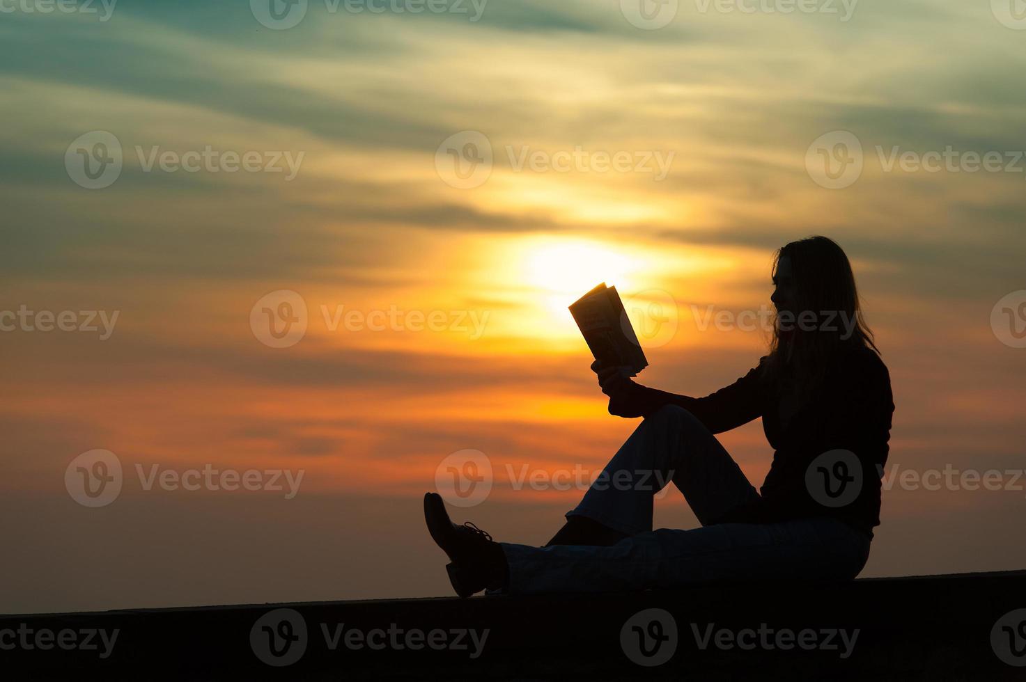 Mädchen, das bei Sonnenuntergang ein Buch an der Wand liest foto