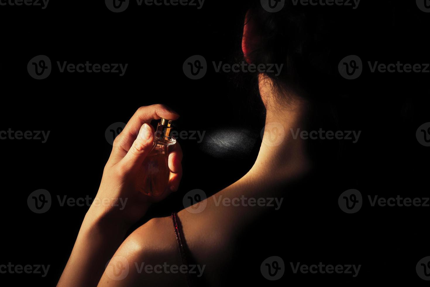 Frau sprüht Parfüm auf ihren Hals mit schwarzem Hintergrund foto