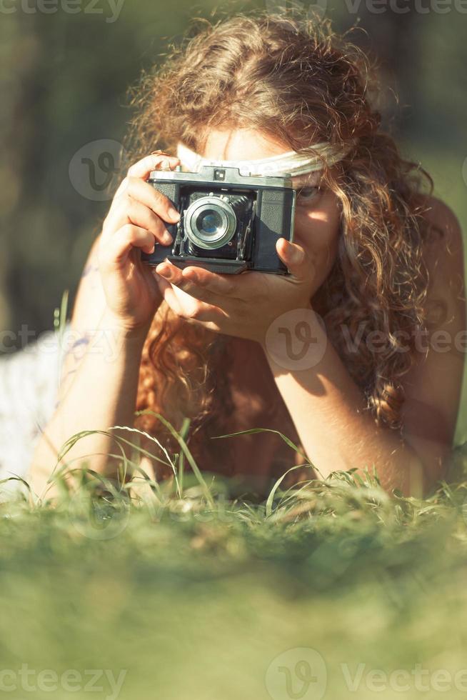 hübsches Hippie-Mädchen auf dem Gras, das Fotos mit einer alten Kamera macht - Vintage-Effekt-Foto