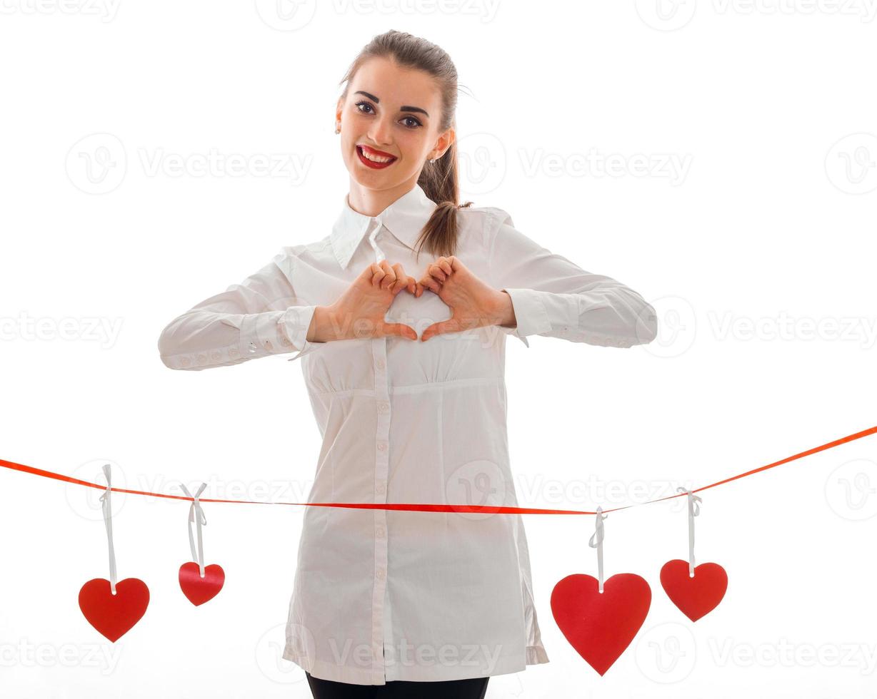 charmante junge brünette Frau mit roten Lippen und Herz im Studio posiert isoliert auf weißem Hintergrund foto