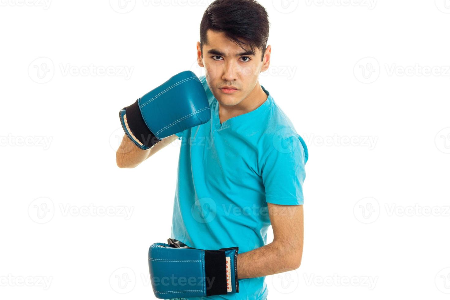 junger wütender brünetter Mann in blauen Boxhandschuhen, der isoliert auf weißem Hintergrund übt foto