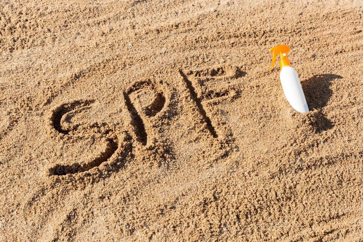 Lichtschutzfaktor. spf-wort geschrieben auf den sand und die weiße flasche mit sonnencreme. hintergrund des hautpflegekonzepts foto