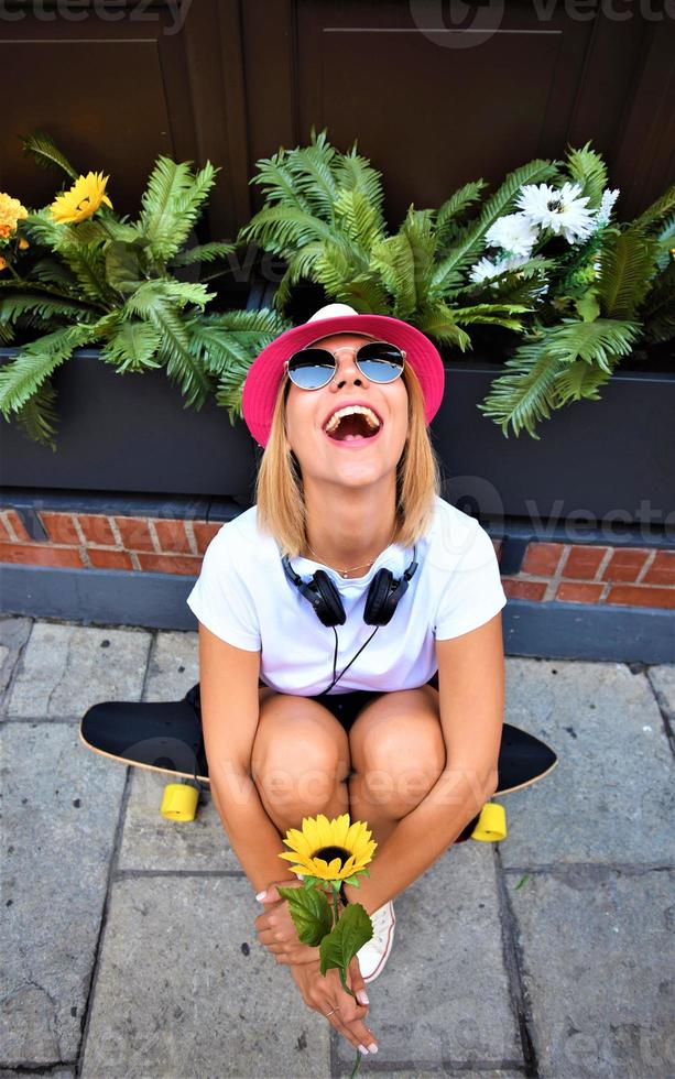 Schönes Hipster-Mädchen mit Skateboard und Sonnenbrille in der Stadt. foto