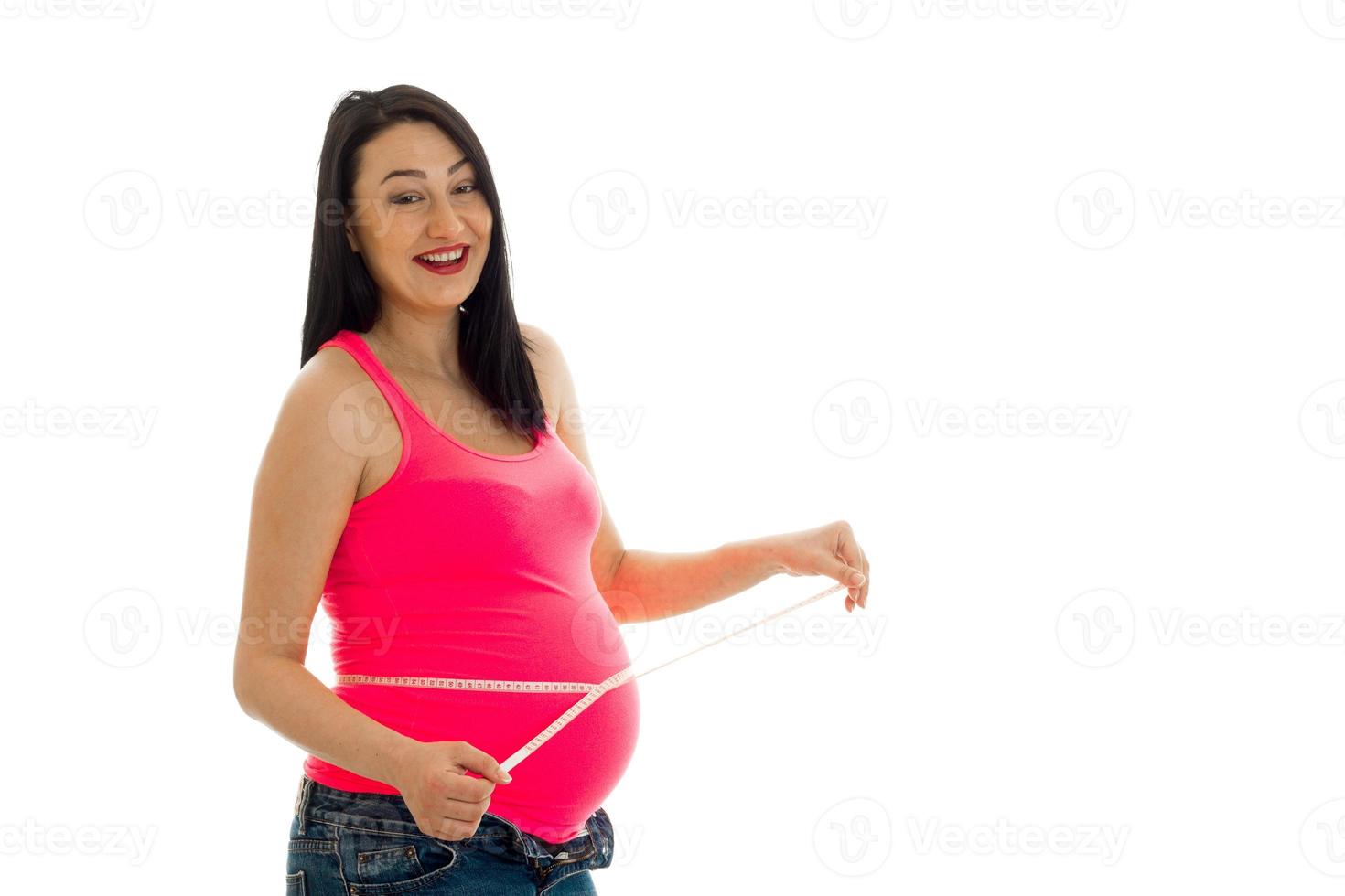 Junge fröhliche schwangere Mutter lacht und misst ihren Bauch isoliert auf weißem Hintergrund im Studio foto