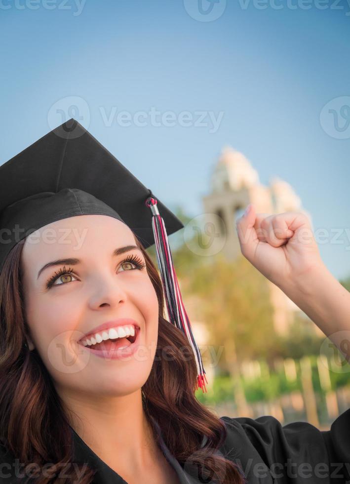 glückliche Abschlussfrau gemischter Abstammung in Mütze und Kleid foto