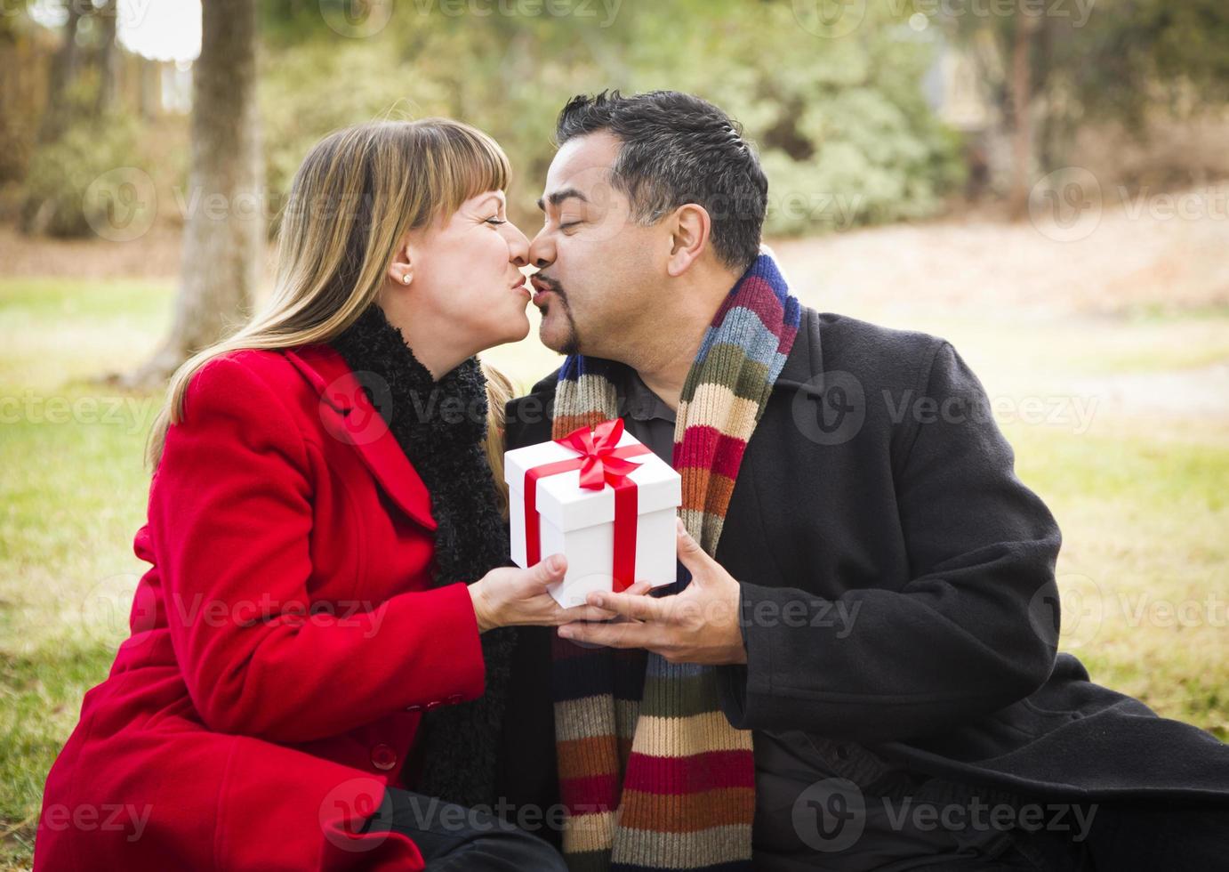 gemischtes rassenpaar, das weihnachts- oder valentinstaggeschenk draußen teilt foto