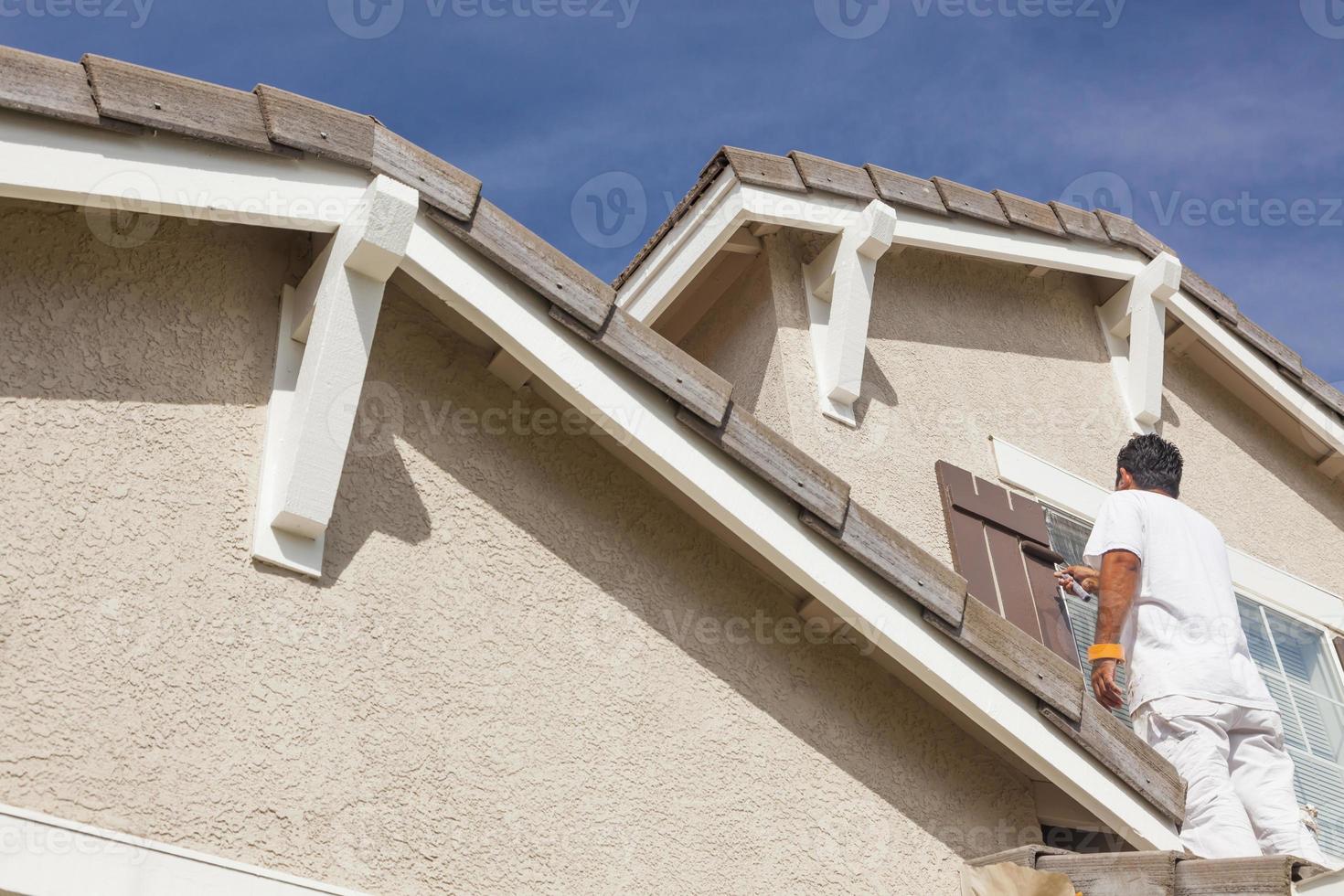 Anstreicher, der die Zierleisten und Fensterläden des Hauses anstreicht foto