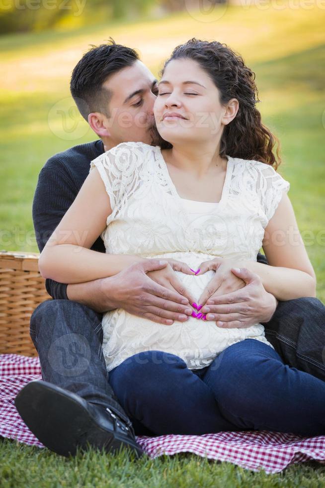 Schwangeres hispanisches Paar, das mit den Händen auf dem Bauch Herzform macht foto