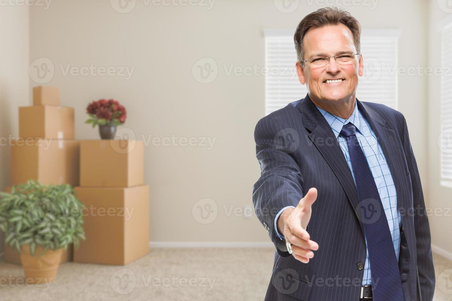 Geschäftsmann, der im Zimmer mit gepackten Kisten nach Handschlag greift foto