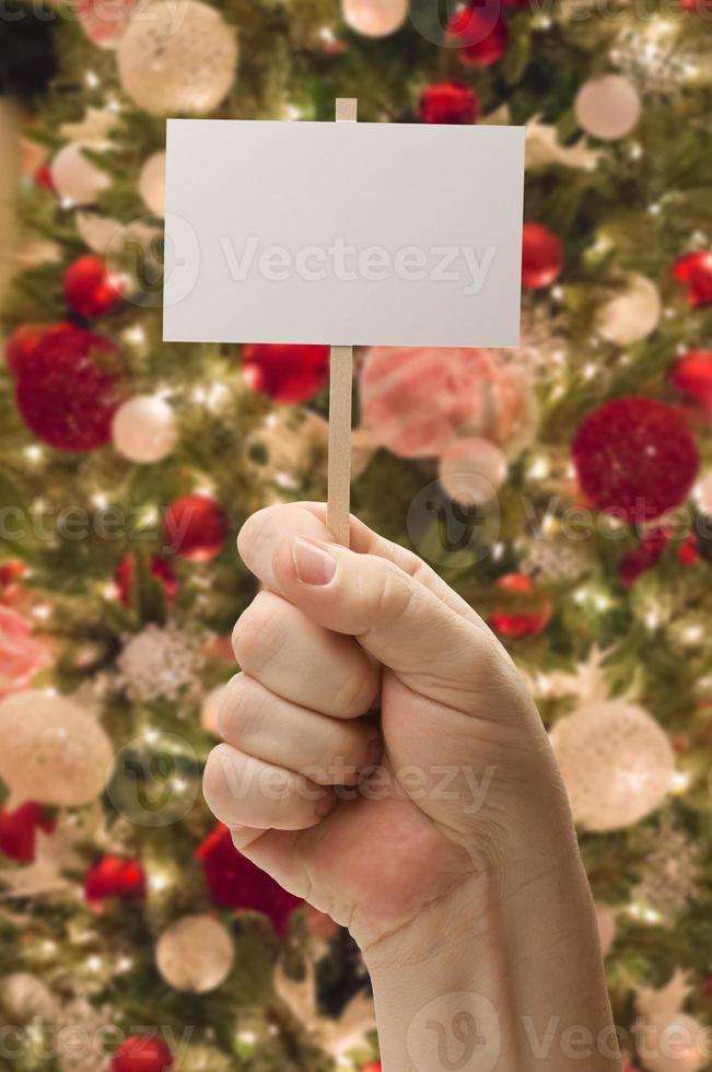 hand, die leere karte vor geschmücktem weihnachtsbaum hält. foto