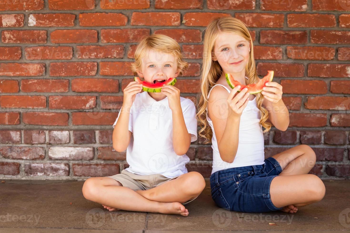 süßer junger cuacasischer junge und mädchen, die wassermelone gegen die mauer essen foto