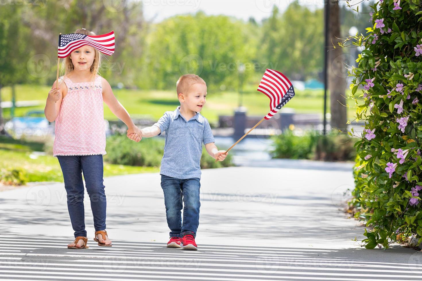 junge schwester und bruder schwenken amerikanische flaggen im park foto