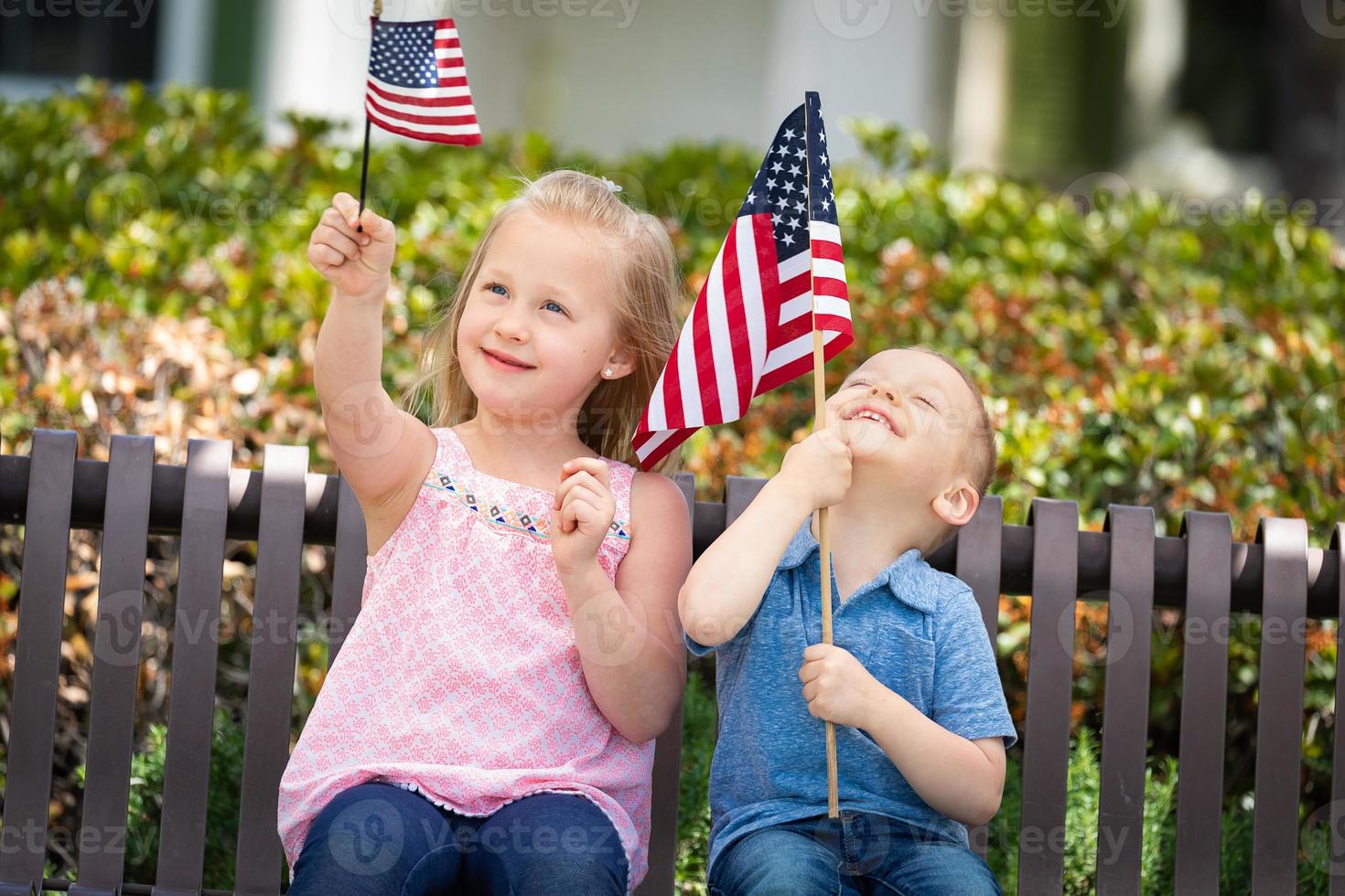 junge schwester und bruder vergleichen sich gegenseitig die größe der amerikanischen flagge auf der bank im park foto