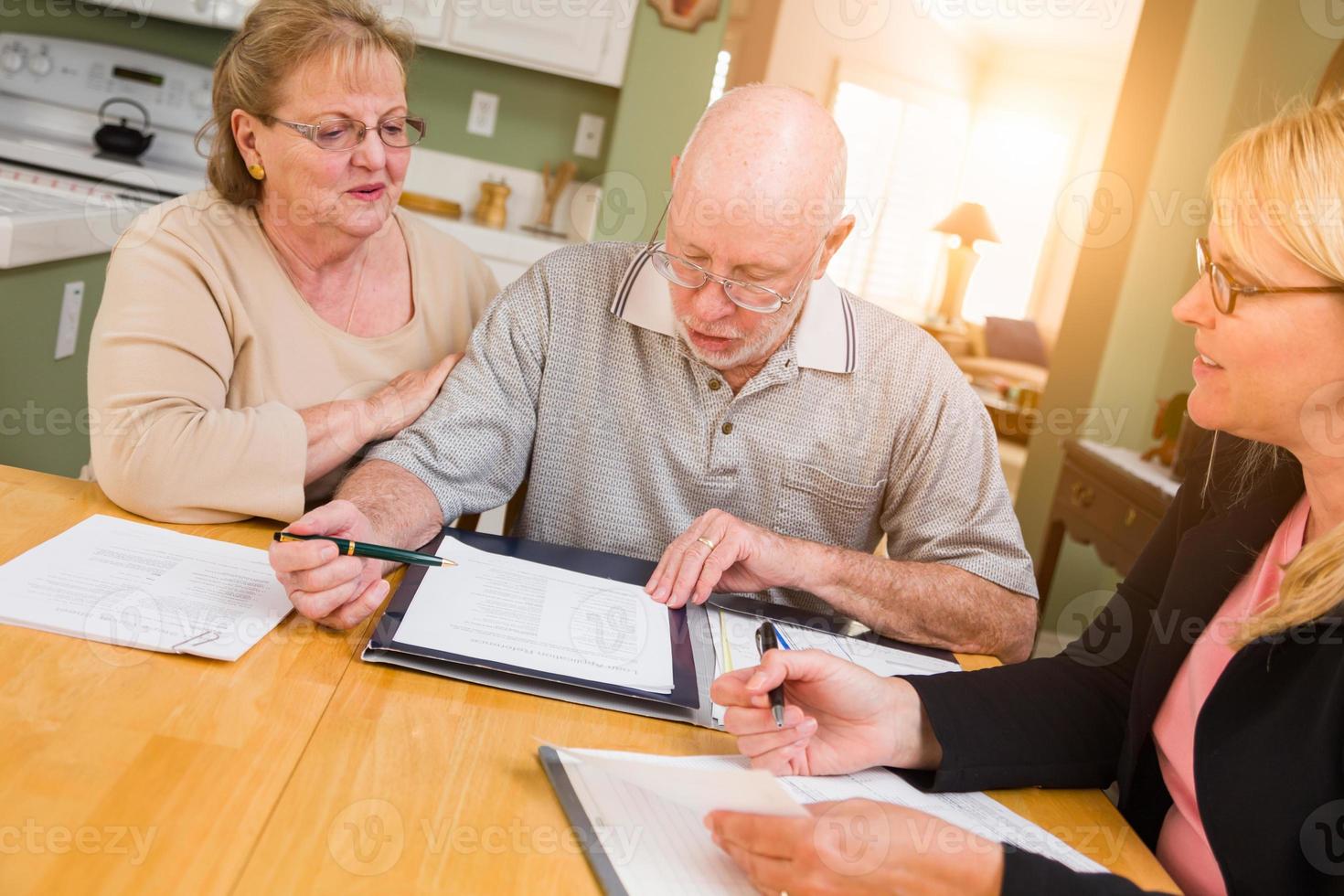 älteres erwachsenes paar, das bei der unterzeichnung dokumente in ihrem haus mit einem agenten durchgeht foto