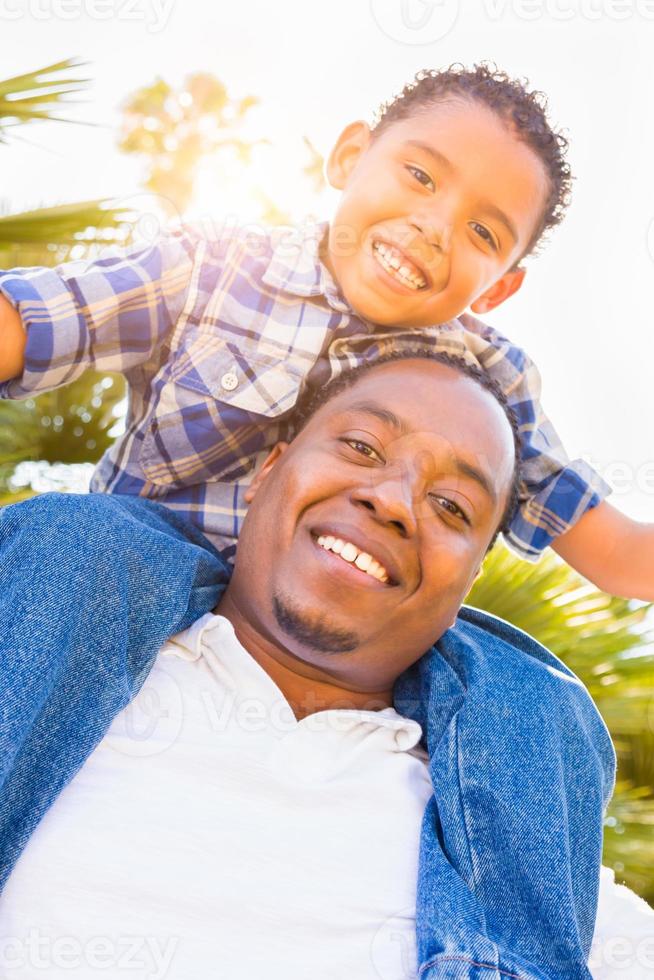 gemischtrassiger sohn und afroamerikanischer vater spielen gemeinsam huckepack im freien. foto