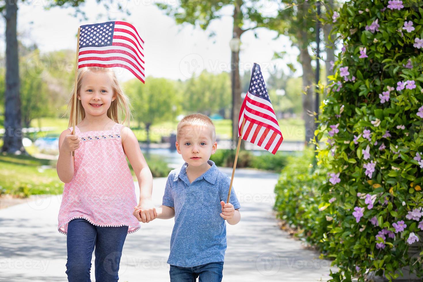 junge schwester und bruder schwenken amerikanische flaggen im park foto