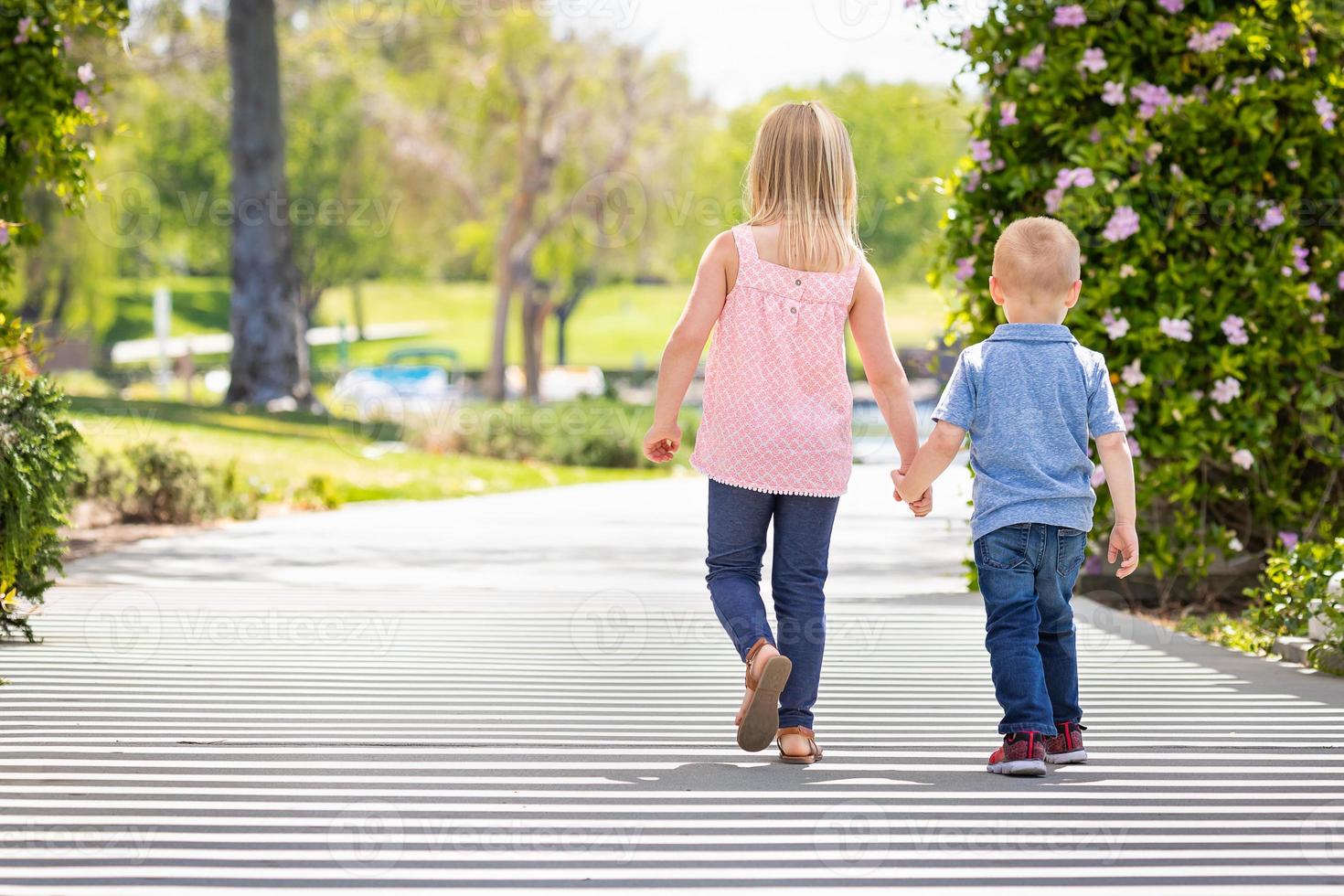 junge schwester und bruder halten sich an den händen und gehen im park spazieren foto