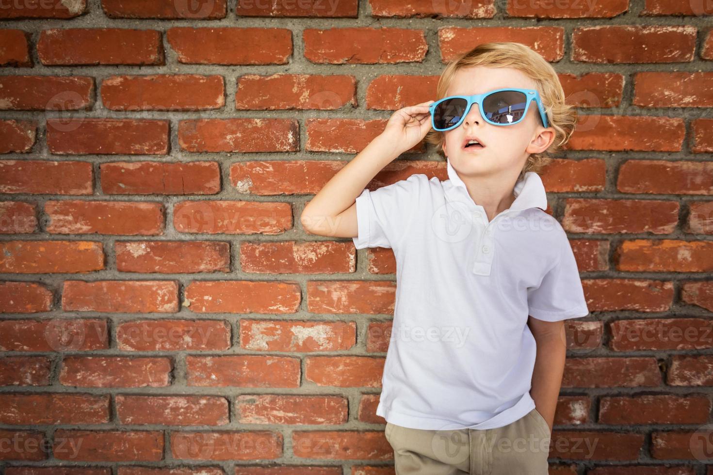 süßer junger kaukasischer Junge mit Sonnenbrille gegen Ziegelwand foto