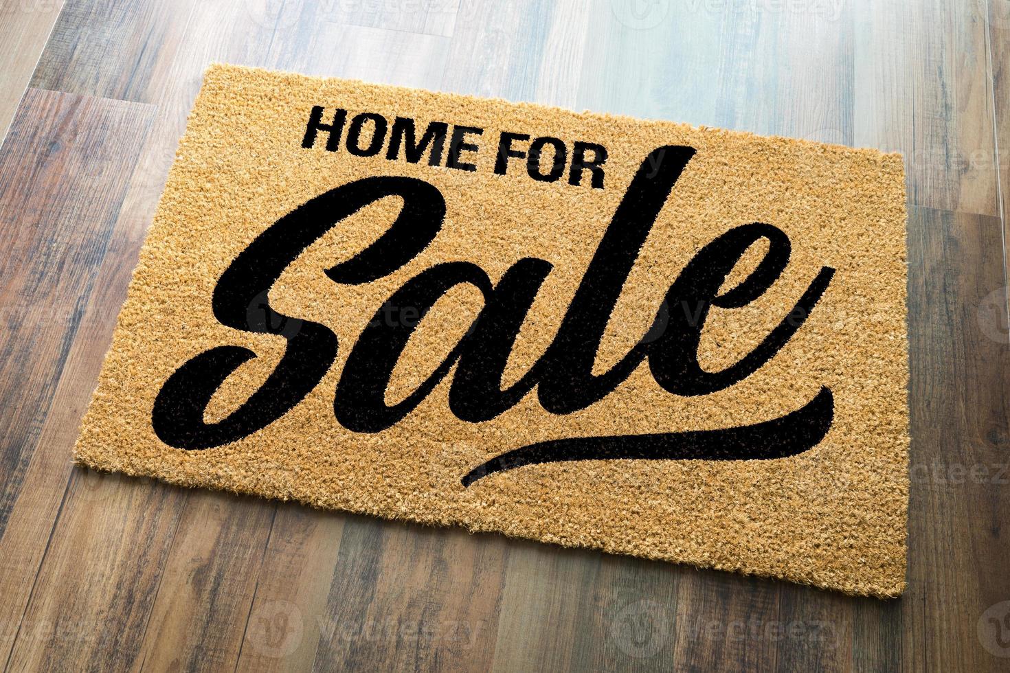 Haus zum Verkauf willkommene Matte auf einem Holzfußbodenhintergrund foto