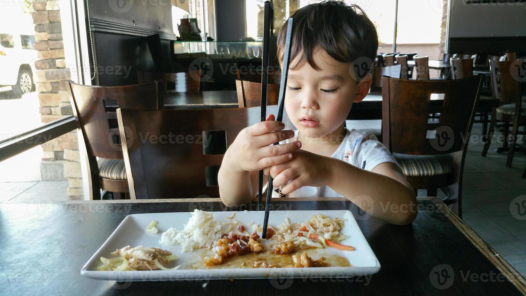 süßer junger chinesischer und kaukasischer junge, der lernt, stäbchen im restaurant zu benutzen foto