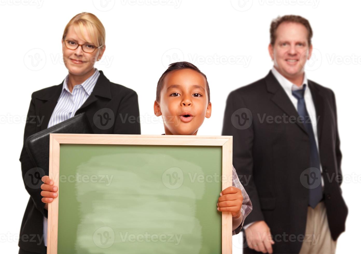 Hispanischer Junge mit Kreidetafel mit Lehrern dahinter foto