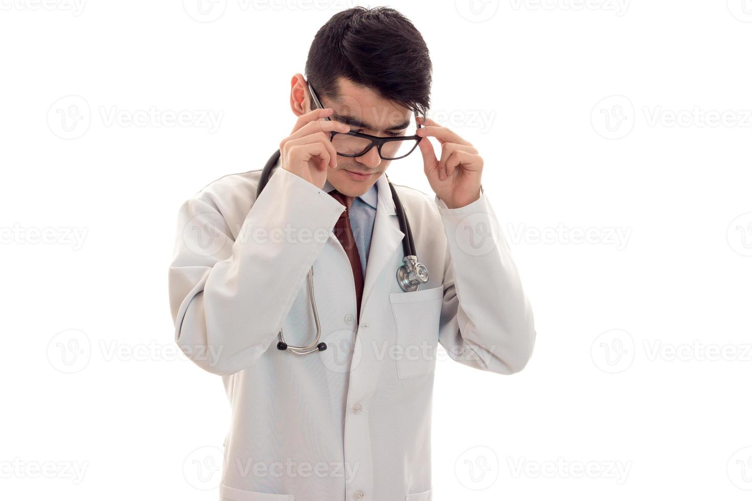 Ein junger Arzt in einem weißen Laborkittel hält die Hände für die Brille isoliert auf weißem Hintergrund foto