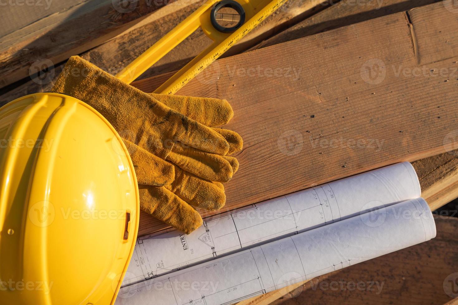 Zusammenfassung von Bauschutzhelmen, Handschuhen, Ebenen- und Hausplänen, die auf Holzplanken ruhen foto