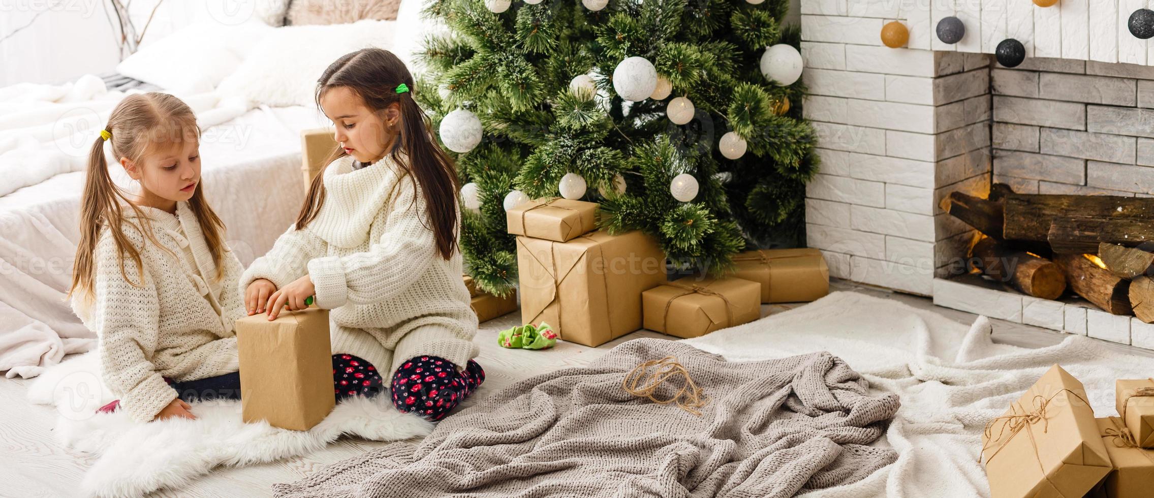 Kinder kleine Schwestern halten Geschenkboxen Innenhintergrund. Was für eine tolle Überraschung. kleine süße Mädchen erhielten Weihnachtsgeschenke. beste Spielzeuge und Weihnachtsgeschenke. Kinderfreunde packen aufgeregt ihre Geschenke aus. foto