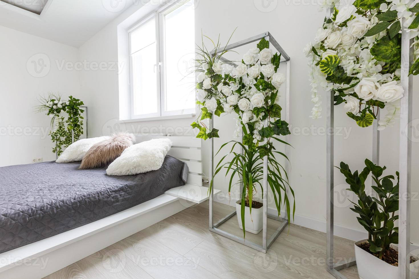 Helles Schlafzimmer mit weißer Wand, großem Bett mit grauer Bettwäsche und handgefertigten Möbeln foto