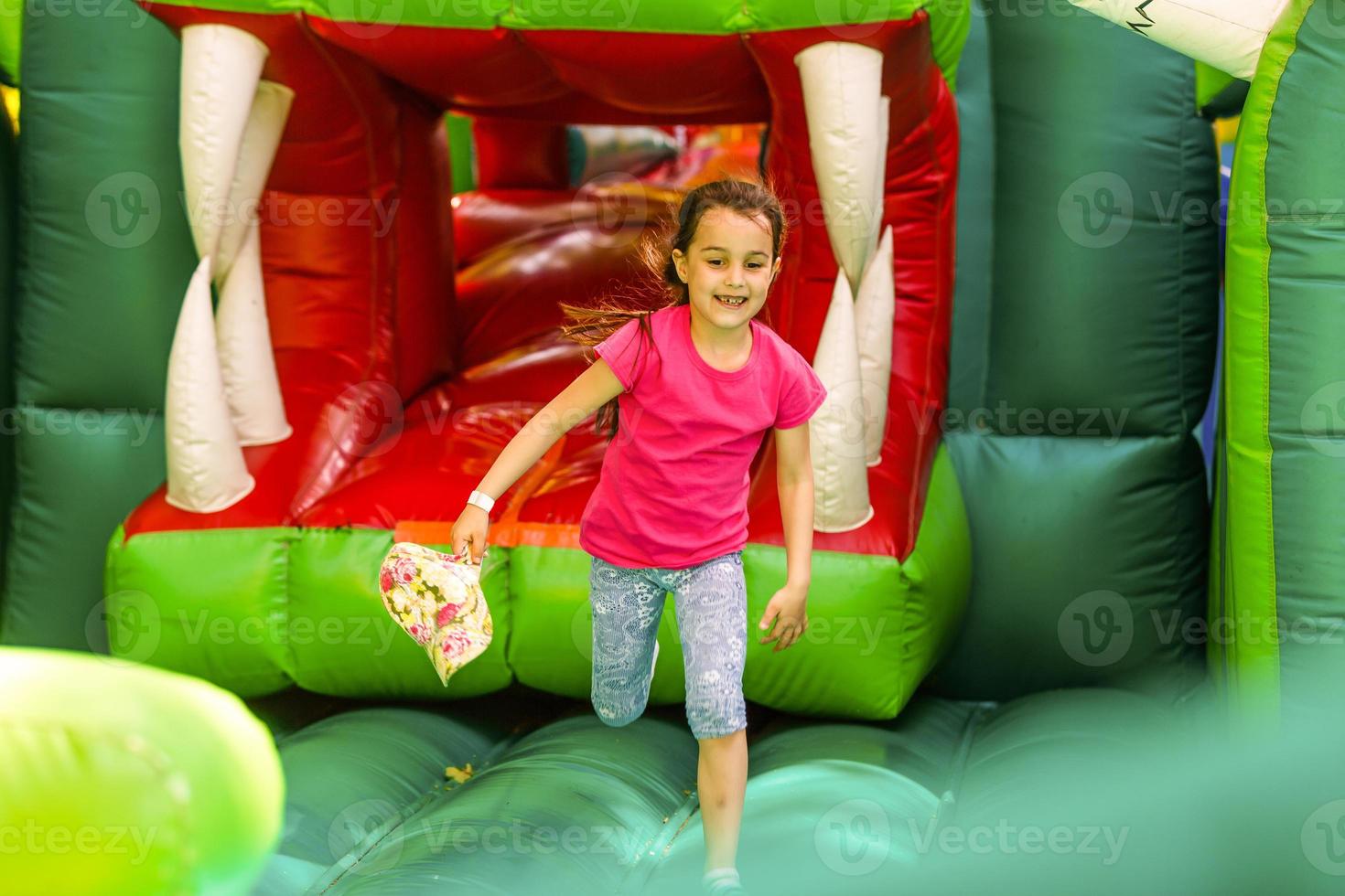 süßes lustiges kleines Mädchen im Vorschulalter in einem bunten, springenden und hüpfenden in einem aufblasbaren Schloss, das sich im Sommer bei einer Kindergeburtstagsfeier auf einem Kinderspielplatz amüsiert foto