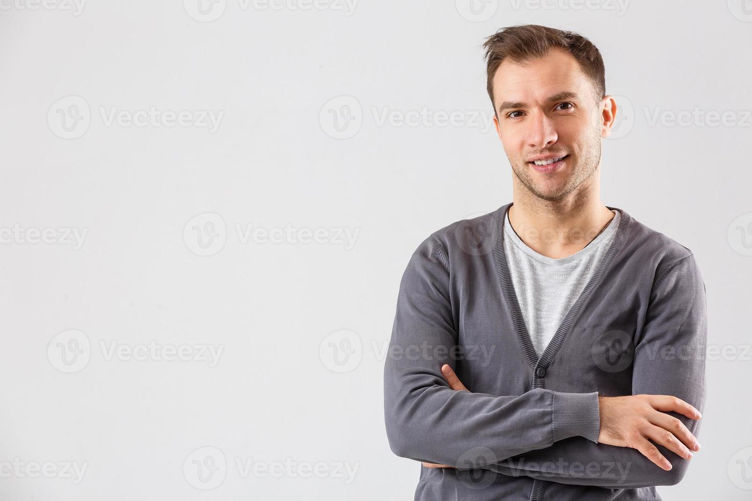 lässig gutaussehend. Selbstbewusster junger gutaussehender Mann, der die Arme verschränkt hält und lächelt, während er vor weißem Hintergrund steht foto