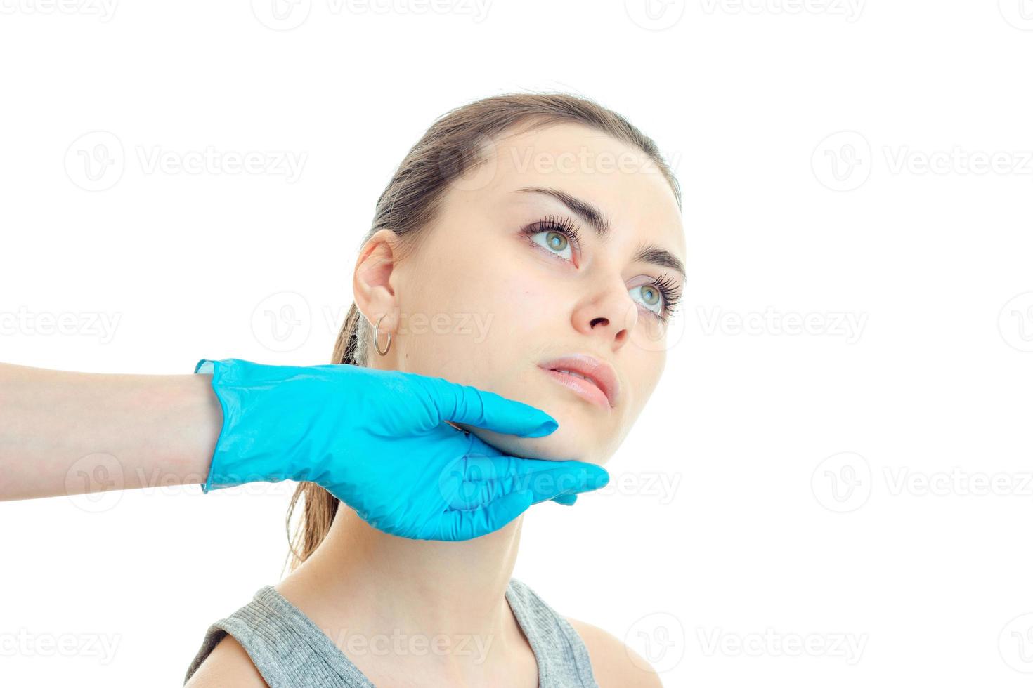 Ein junges Mädchen bei einer Kosmetikerin, das ihr Gesicht mit der Hand in einem blauen Handschuh aus nächster Nähe überprüft foto
