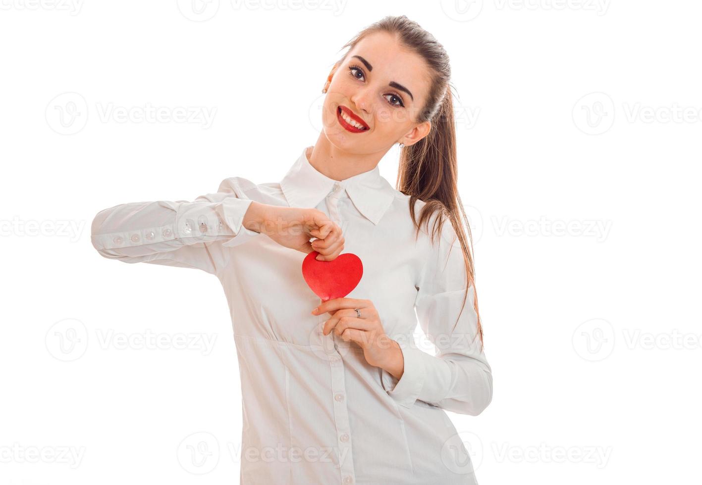 Junge, fröhliche Frau mit roten Lippen, die sich darauf vorbereitet, den Valentinstag mit Herzsymbol im Studio zu feiern, isoliert auf weißem Hintergrund foto