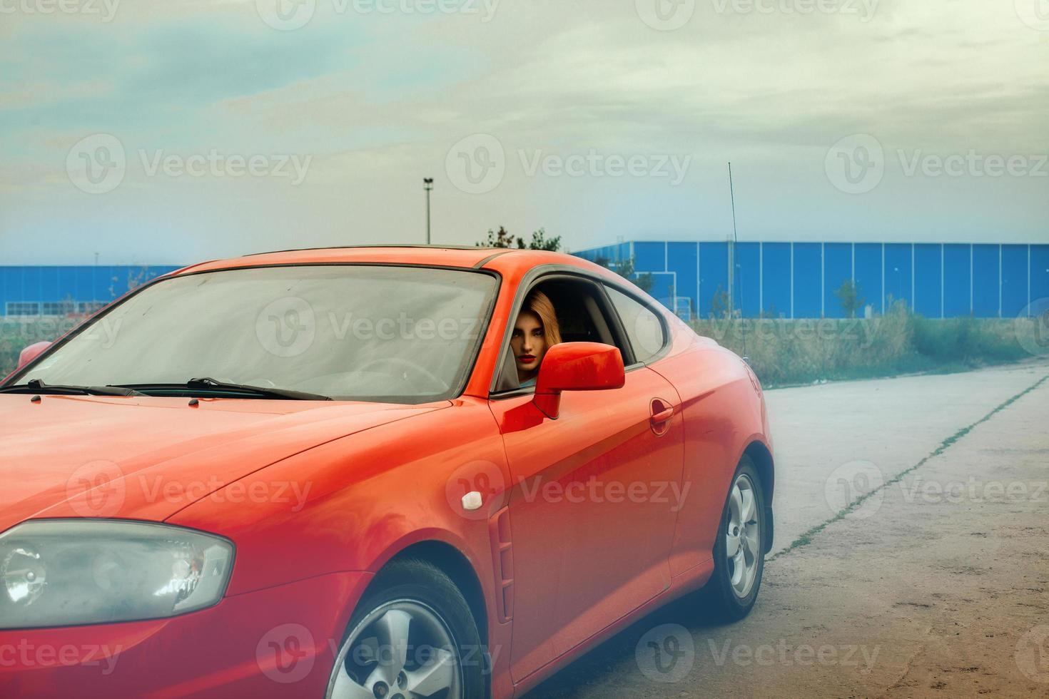 Frau mit roten Lippen, die ein rotes Auto fährt foto