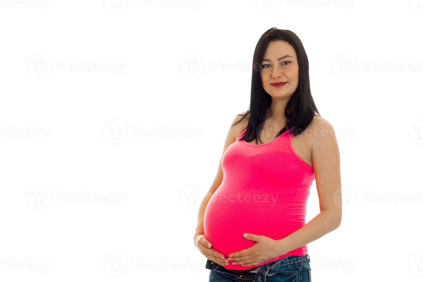 schöne junge schwangere frau in einem rosa t-shirt hält hände bauch foto