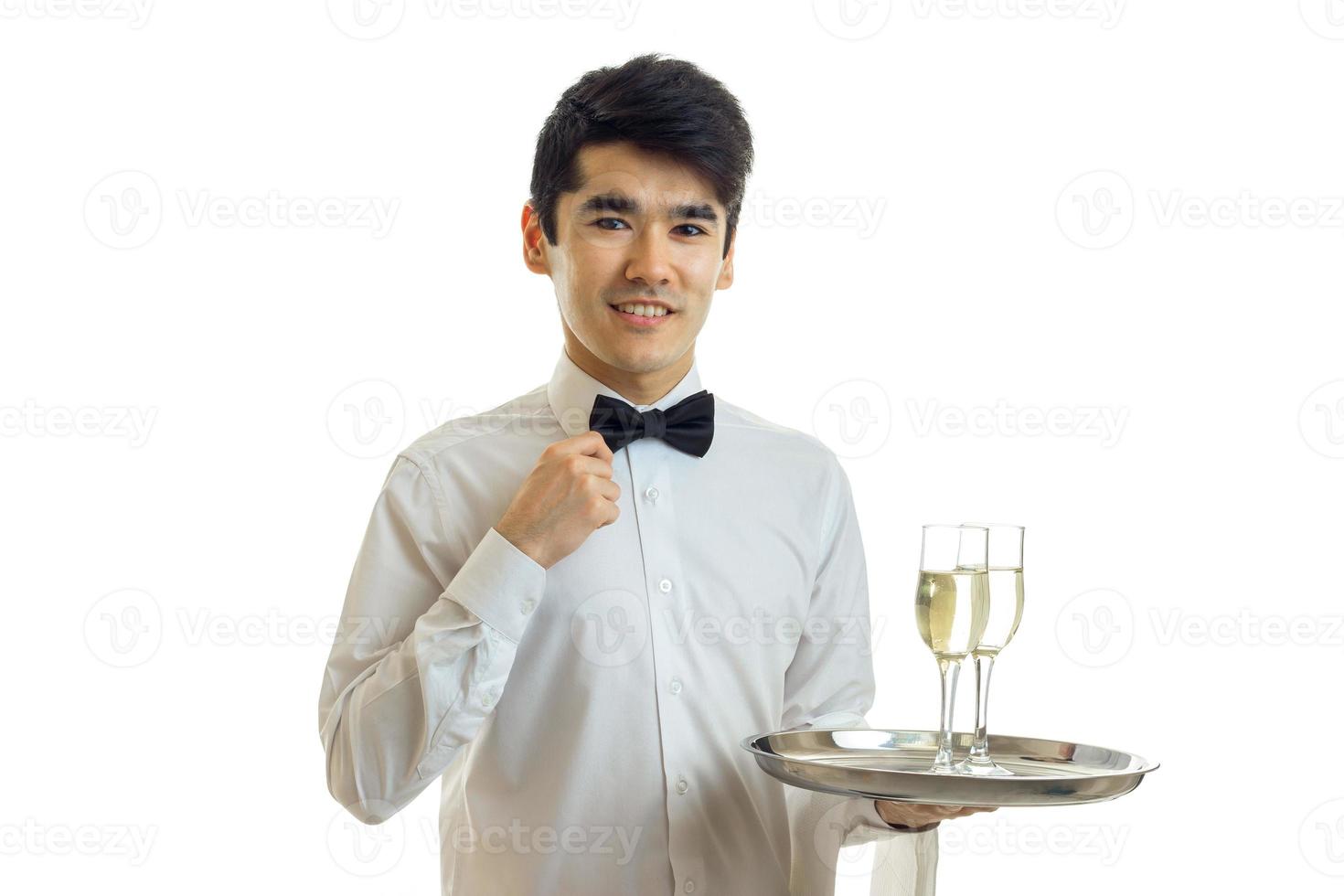 gutaussehender junger Kellner in einem weißen Hemd, der lächelt und zwei Gläser Champagner auf einem Tablett hält foto