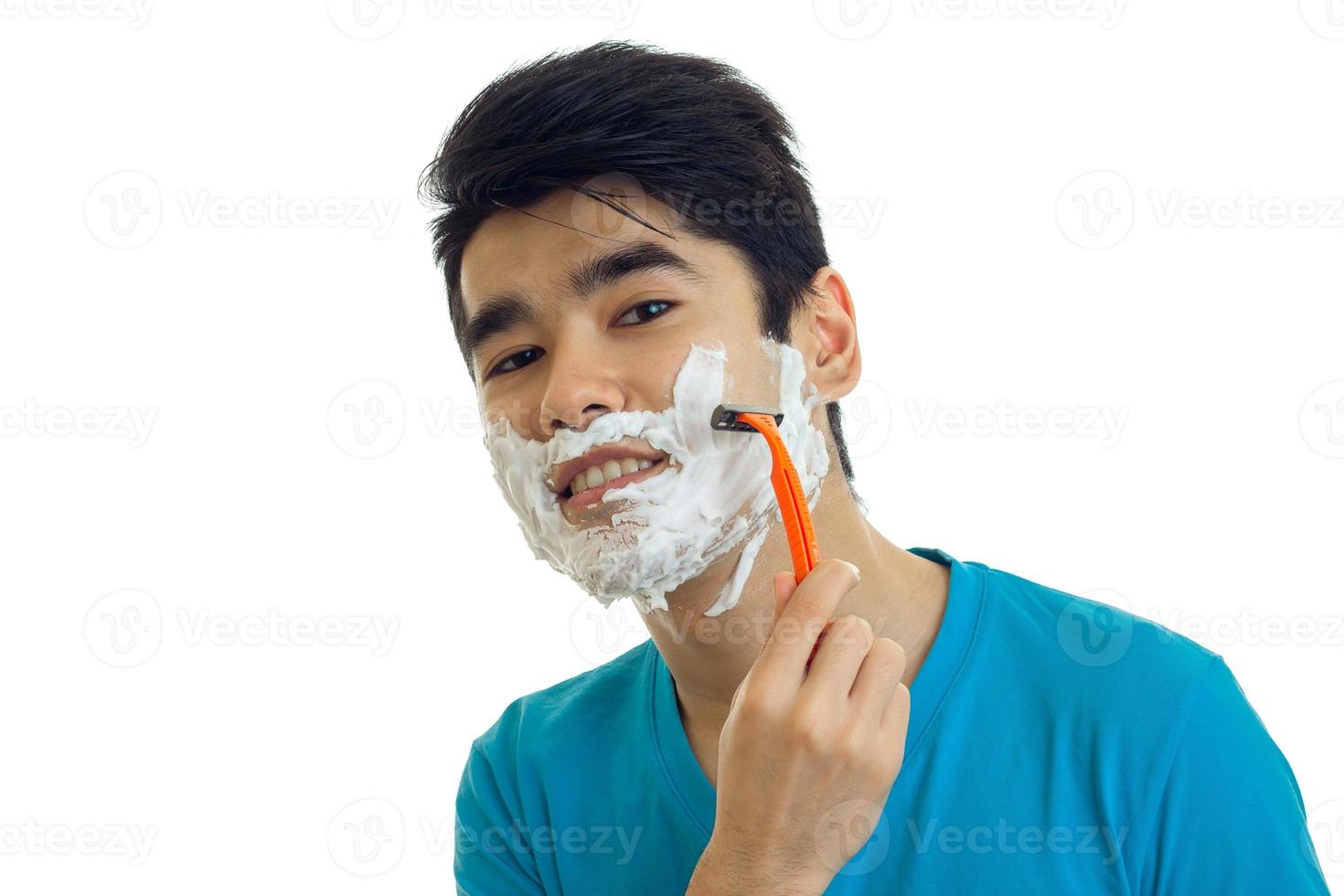 Porträt eines lächelnden jungen Mannes mit Schaum im Gesicht, der sich den Bart rasiert und aus nächster Nähe in die Kamera schaut foto