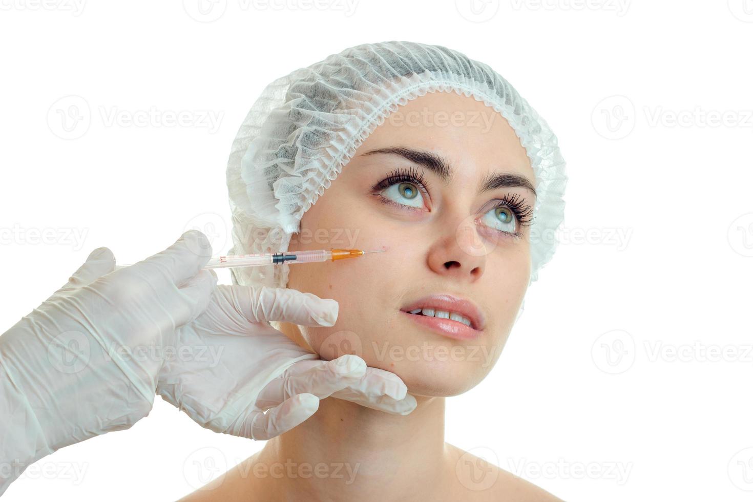 junges mädchen ohne make-up in der medizinischen kappe hob die augen und die kosmetikerin macht ihren stich ins gesicht aus der nähe foto
