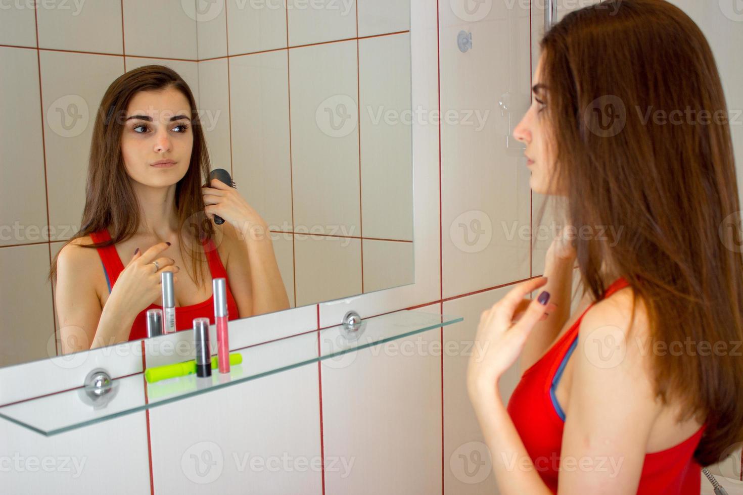 charmantes junges mädchen steht vor einem spiegel und hält in der hand einen haarkamm foto