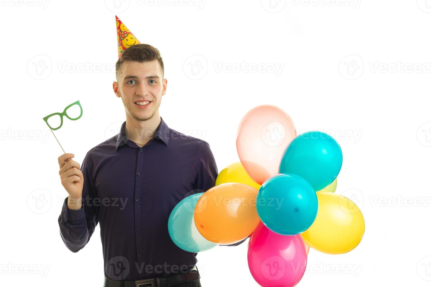 Fröhlicher Typ auf einer Geburtstagsfeier mit Papierbrille und Luftballons in den Händen foto