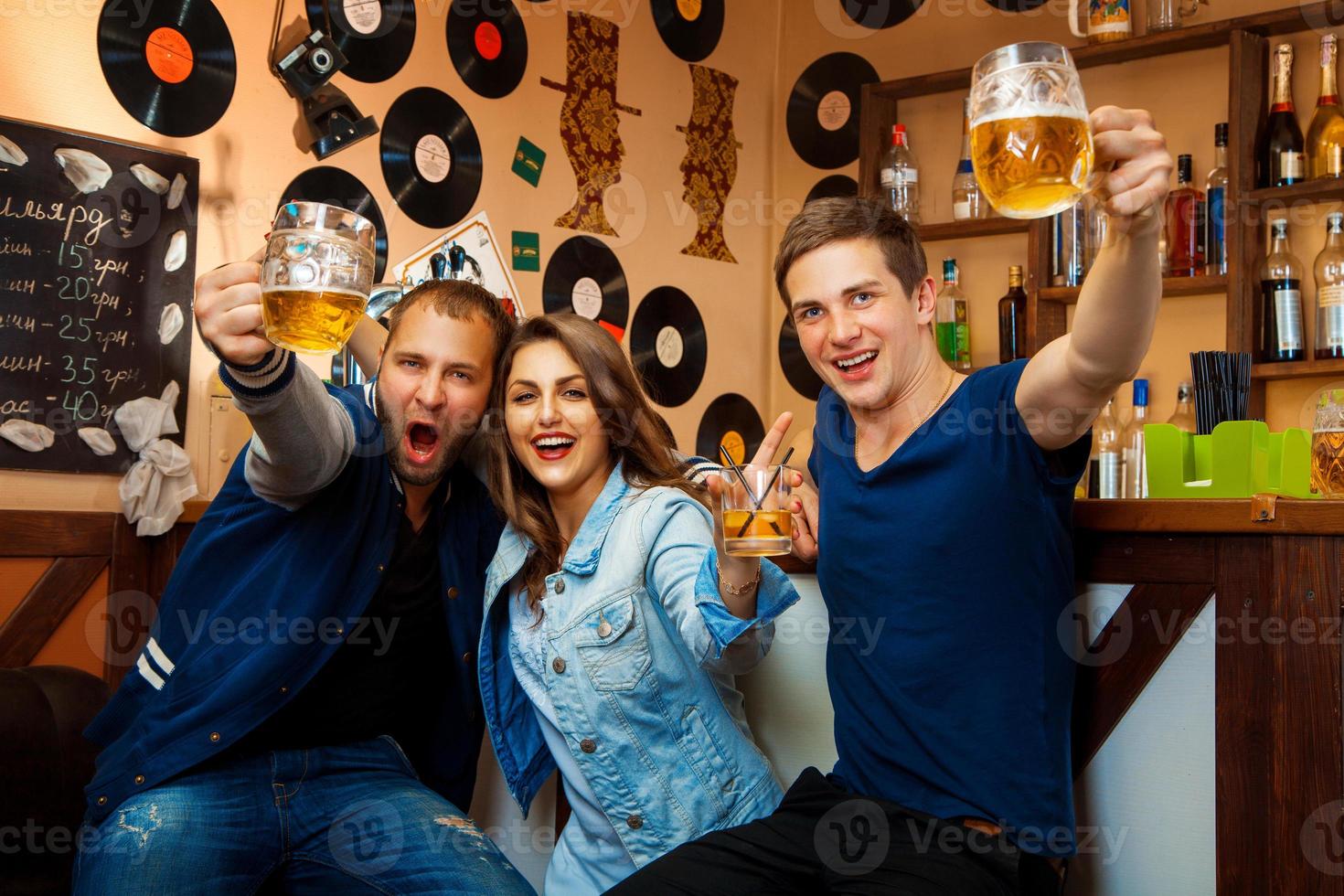 lustige Gesellschaft von zwei Jungen und einem Mädchen trinken in der Bar foto