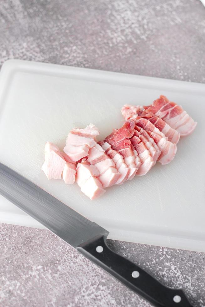 durchwachsenes schweinefleisch wird auf einem weißen schneidebrett in der küche geschnitten. nahaufnahme schnittfolie schweinebauch roh foto