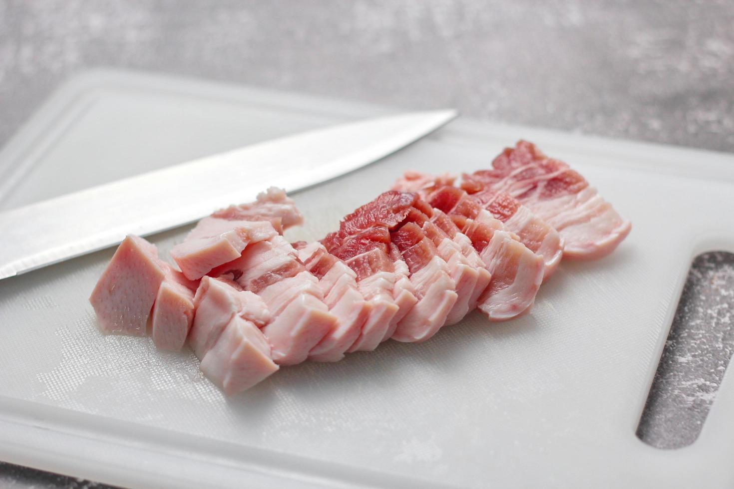 durchwachsenes schweinefleisch wird auf einem weißen schneidebrett in der küche geschnitten. nahaufnahme schnittfolie schweinebauch roh foto